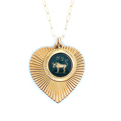 A gold ribbed heart-shaped pendant necklace with a Taurus zodiac bull design in dark teal enamel center on a gold paperclip chain against a white background