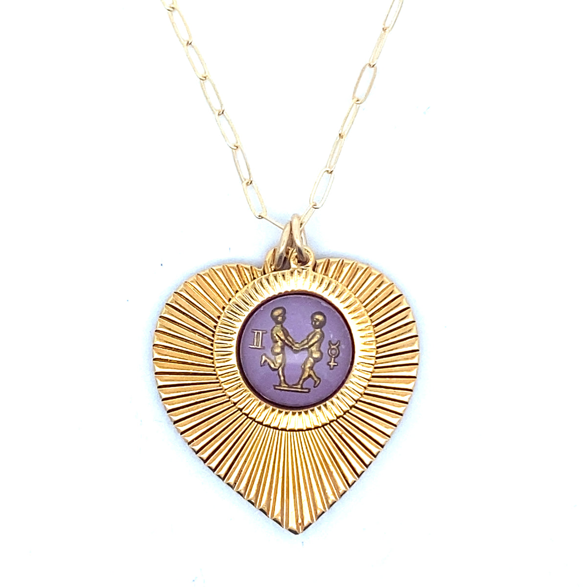 A gold ribbed heart-shaped pendant necklace with a Gemini zodiac twins design in purple enamel center on a gold paperclip chain against a white background
