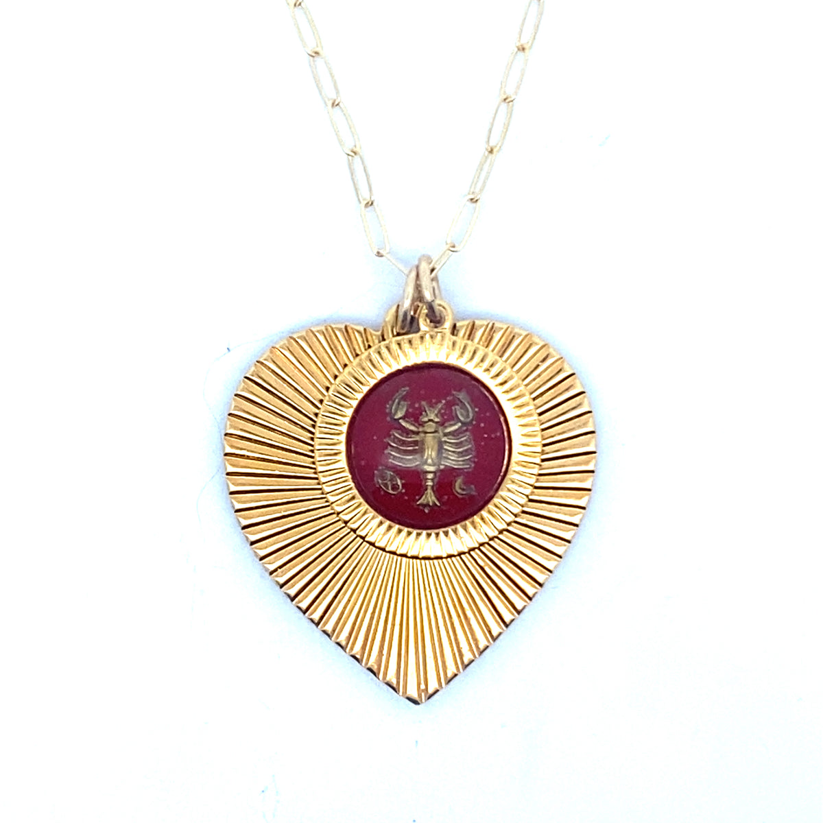 A gold ribbed heart-shaped pendant necklace with a Cancer zodiac crab design in burgundy enamel center on a gold paperclip chain against a white background