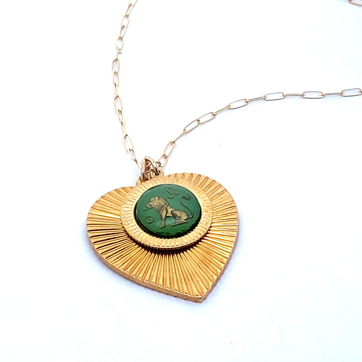 A gold ribbed heart-shaped pendant necklace with a Leo zodiac lion design in green enamel center on a gold paperclip chain against a white background
