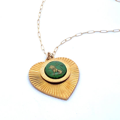 A gold ribbed heart-shaped pendant necklace with a Leo zodiac lion design in green enamel center on a gold paperclip chain against a white background