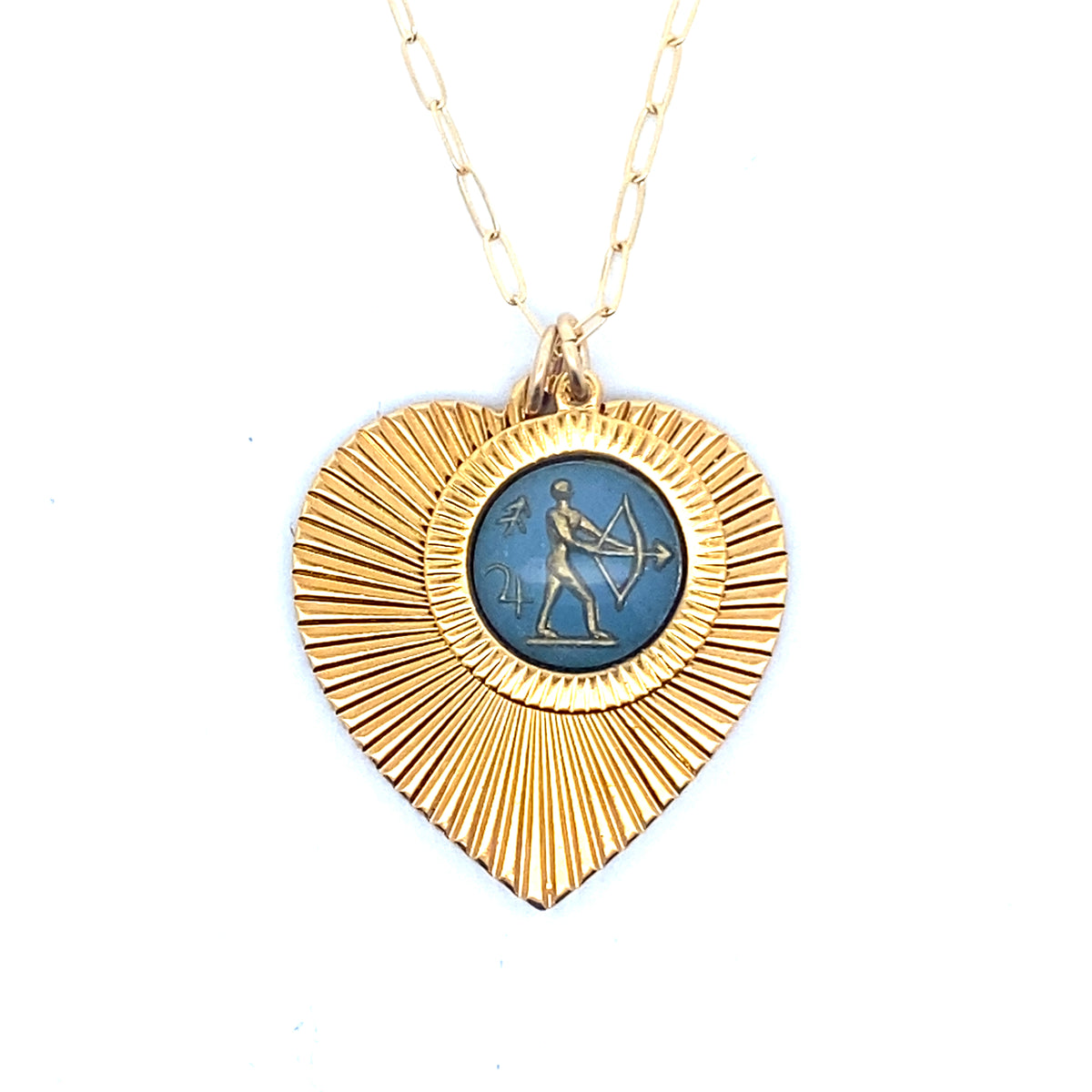 A gold ribbed heart-shaped pendant necklace with a Sagittarius zodiac archer design in blue enamel center on a gold paperclip chain against a white background