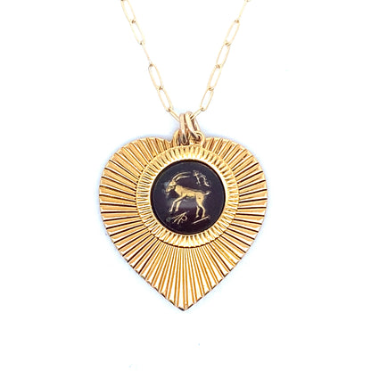A gold ribbed heart-shaped pendant necklace with a Capricorn zodiac goat design in black enamel center on a gold paperclip chain against a white background