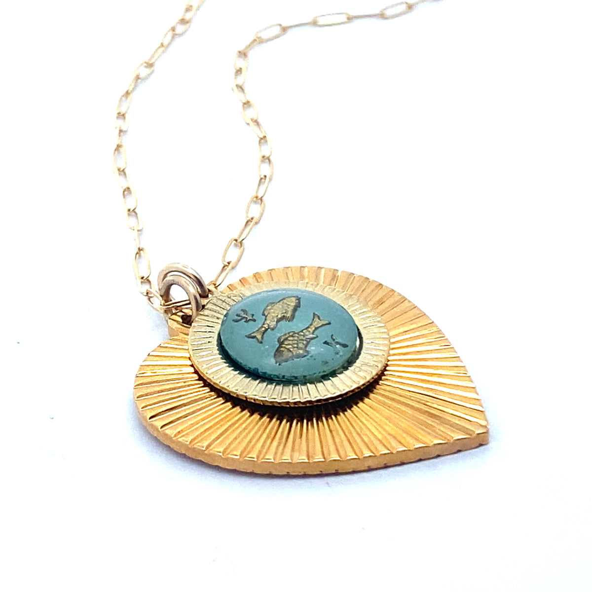 A gold ribbed heart-shaped pendant necklace with a Pisces zodiac fish design in teal enamel center on a gold paperclip chain against a white background