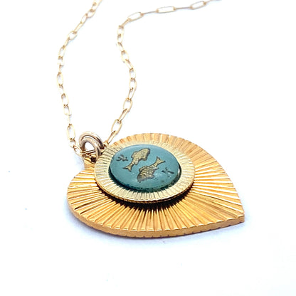 A gold ribbed heart-shaped pendant necklace with a Pisces zodiac fish design in teal enamel center on a gold paperclip chain against a white background