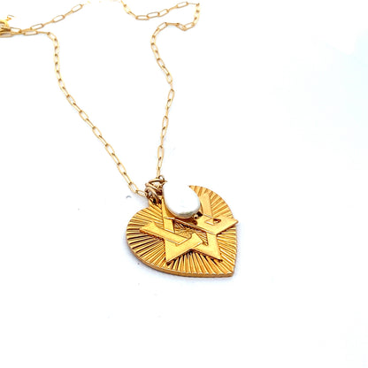Angled view of a gold ribbed heart pendant with Star of David design and pearl moonstone accent on a gold paperclip chain against a white background