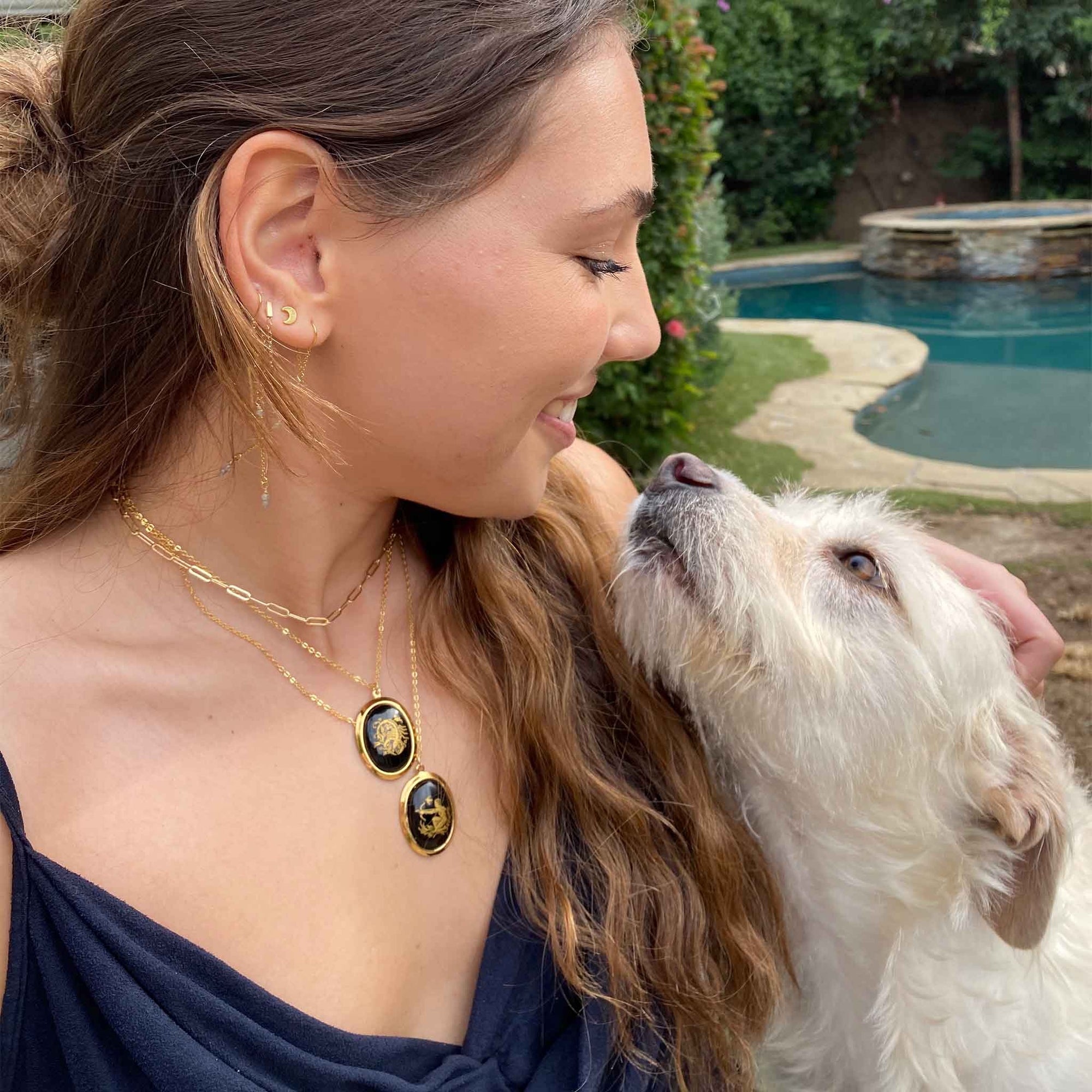 lifestyle shot of woman wearing two layered gold-plated necklaces with two vintage black and gold glass zodiac sign charms