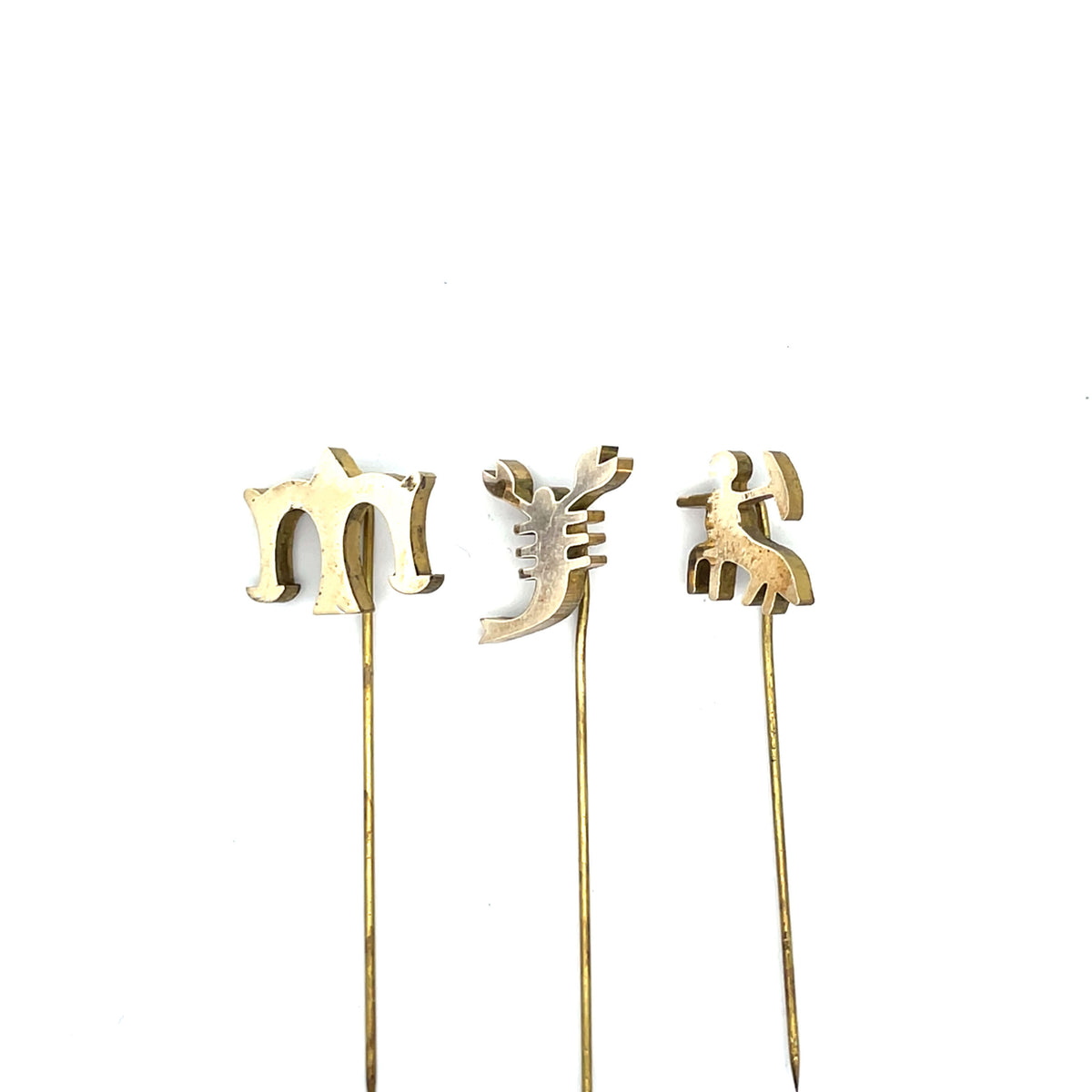 Three gold cake toppers shaped like letters on sticks against a white background