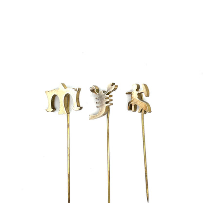 Three gold cake toppers shaped like letters on sticks against a white background