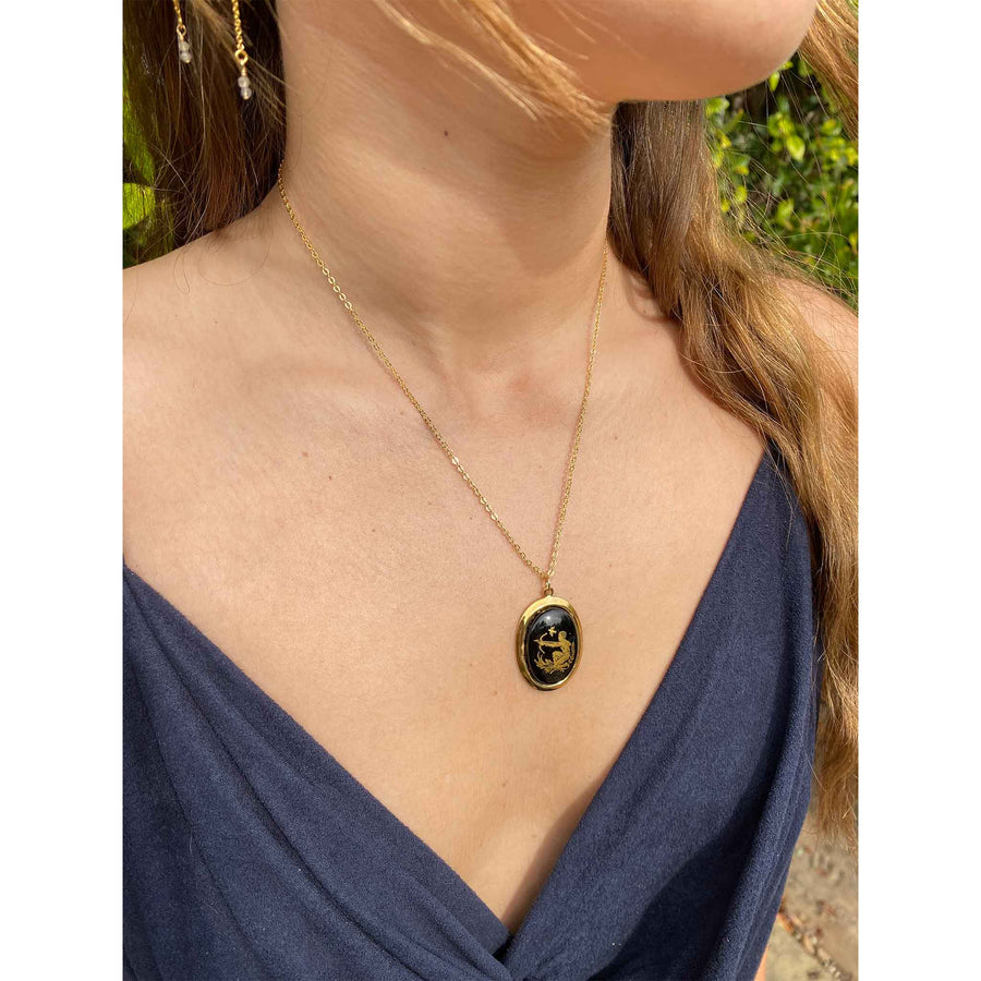 lifestyle shot of woman wearing a gold-plated necklace with a vintage black and gold glass zodiac sign charm