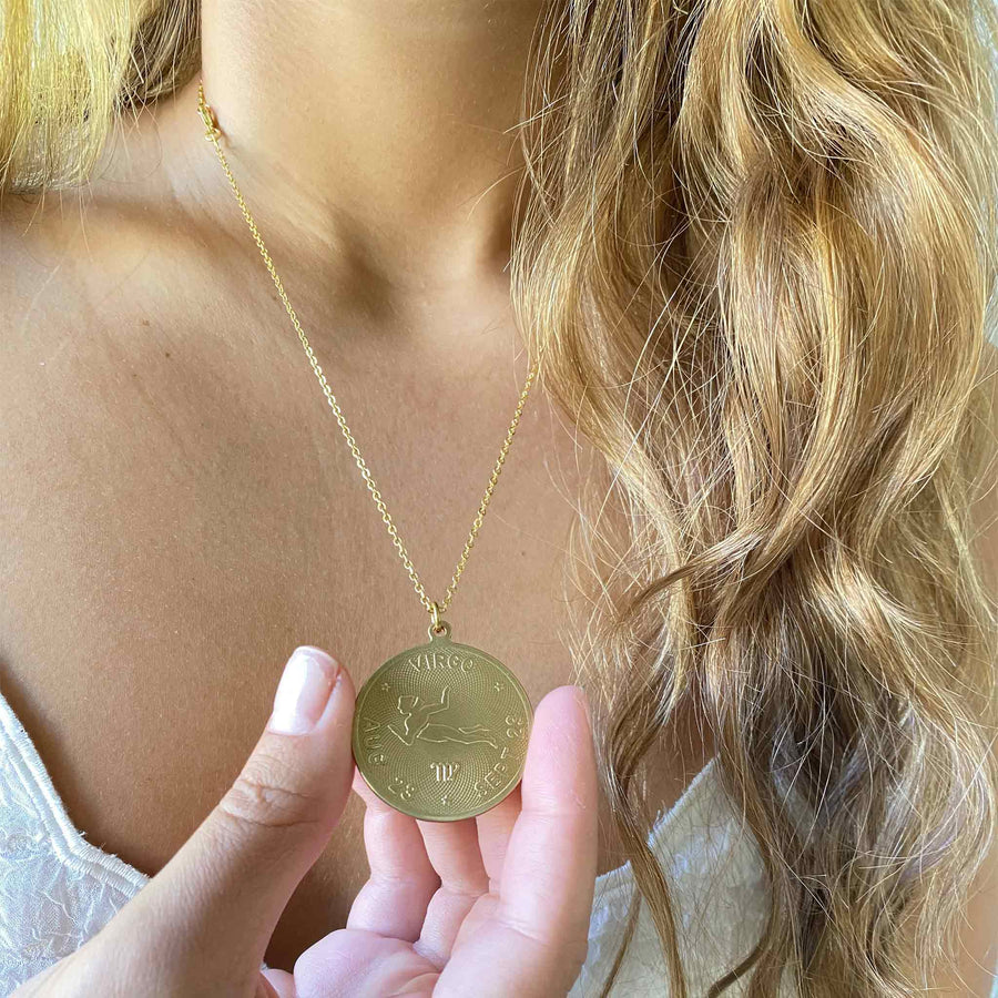 close up image of a virgo vintage brass coin zodiac sign charm hung on a necklace 