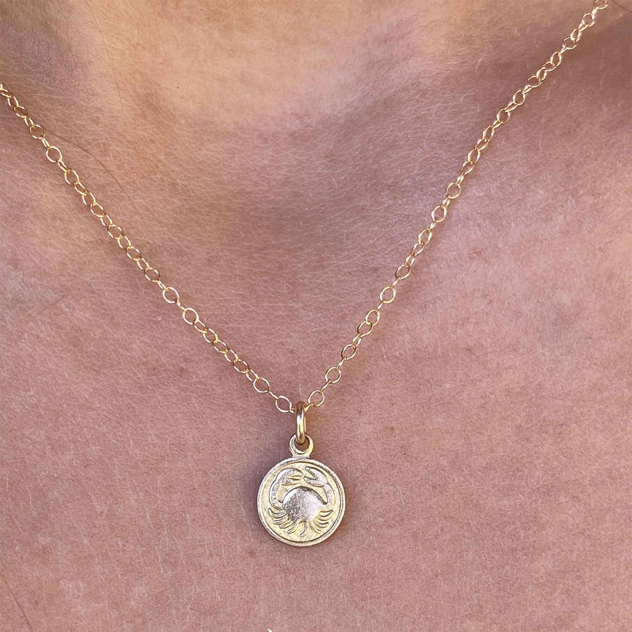 closeup of woman wearing a necklace with a tiny vintage Cancer zodiac sign charm